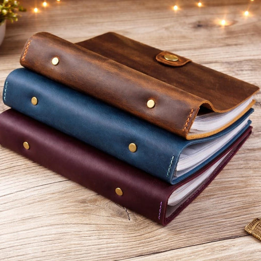Three leather-bound photo album stacked on a wooden surface with decorative lights in the background.