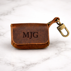 Brown leather keychain pouch with 'MJG' engraving on a marble surface