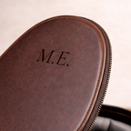 Brown leather case with 'M.E.' monogram on a wooden surface