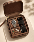 Brown jewelry case with a watch, sunglasses, and earrings on a beige background