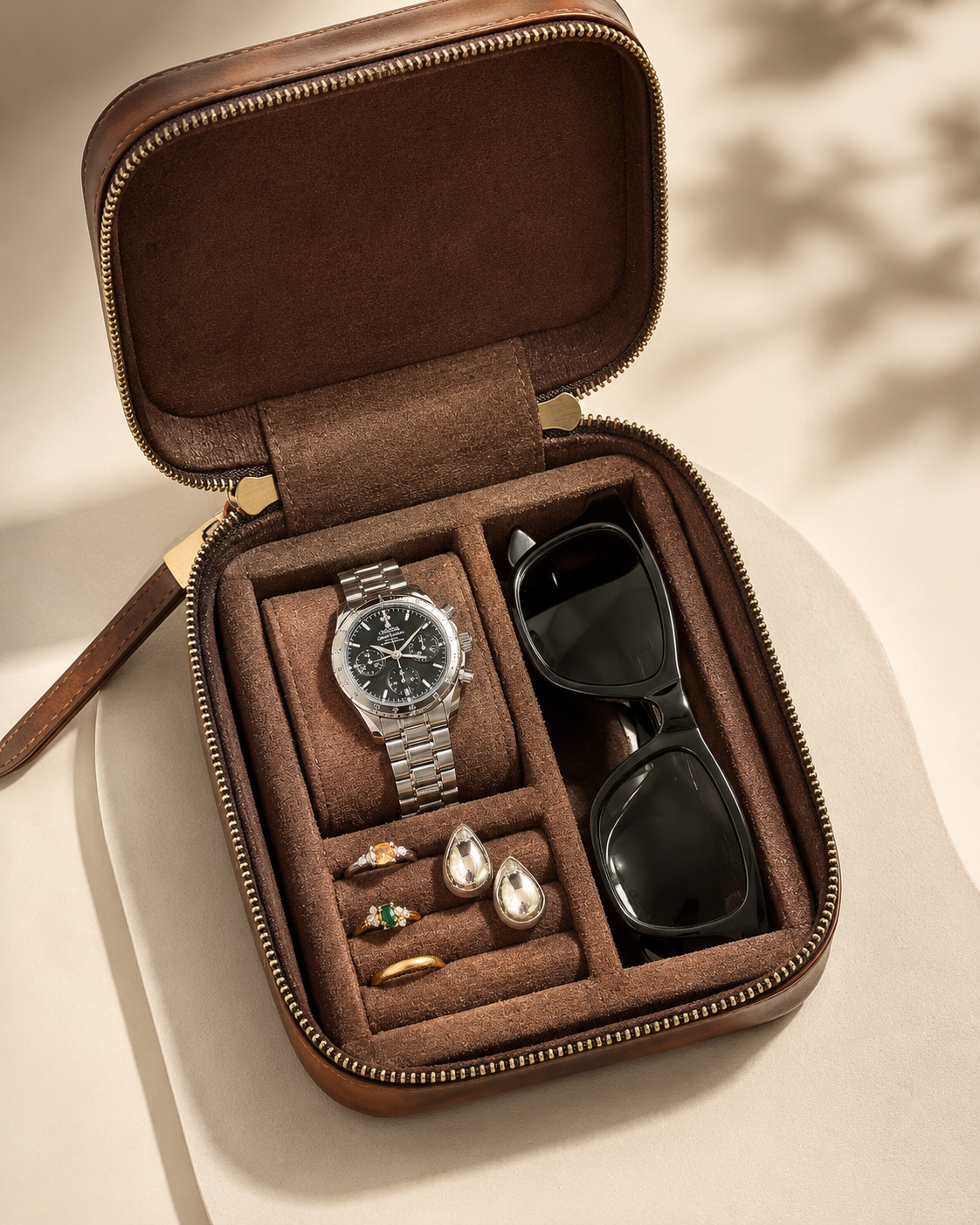 Brown jewelry case with a watch, sunglasses, and earrings on a beige background