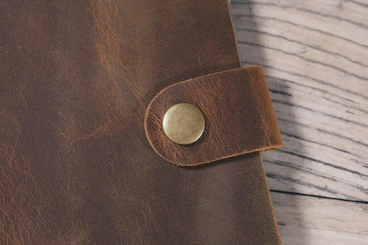 Close-up of a brown leather strap with a metal buckle on a wooden surface
Three leather-bound photo album stacked on a wooden surface with decorative lights in the background.