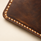 Close-up of distressed full-grain brown leather wallet edge with tan saddle stitching