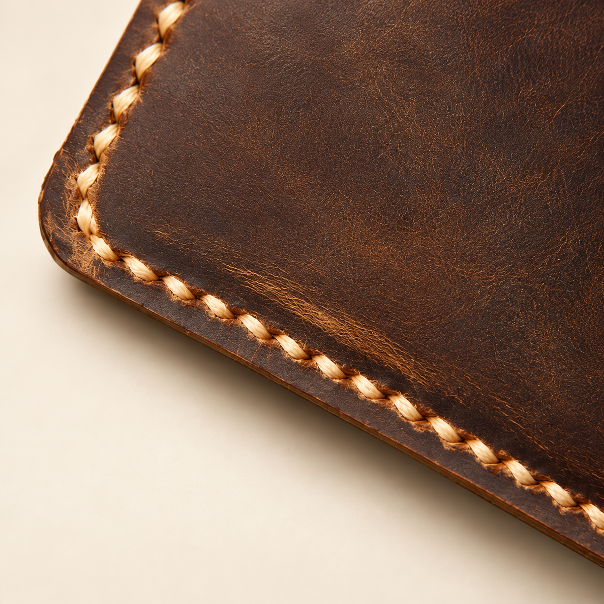 Close-up of distressed full-grain brown leather wallet edge with tan saddle stitching